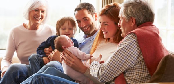 Multi Generation Family Sitting On Sofa With Newborn Baby